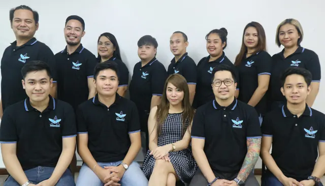 Group of thirteen Alliance Global Solutions team members posing in two rows; most wear black company polo shirts with the AGS logo