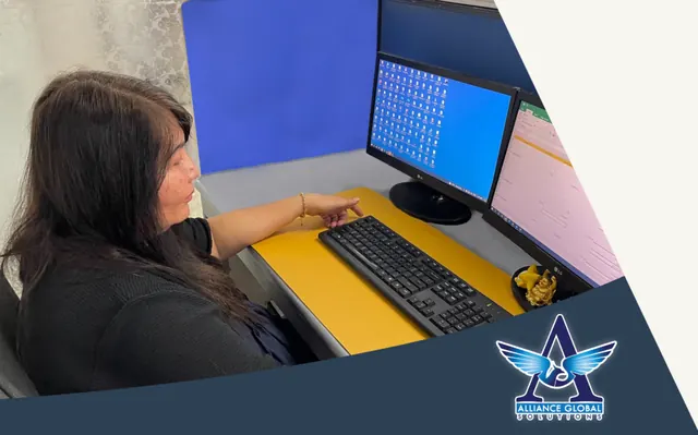 Alliance Global Solutions team member working at a dual-monitor desk with a spreadsheet open in an office cubicle